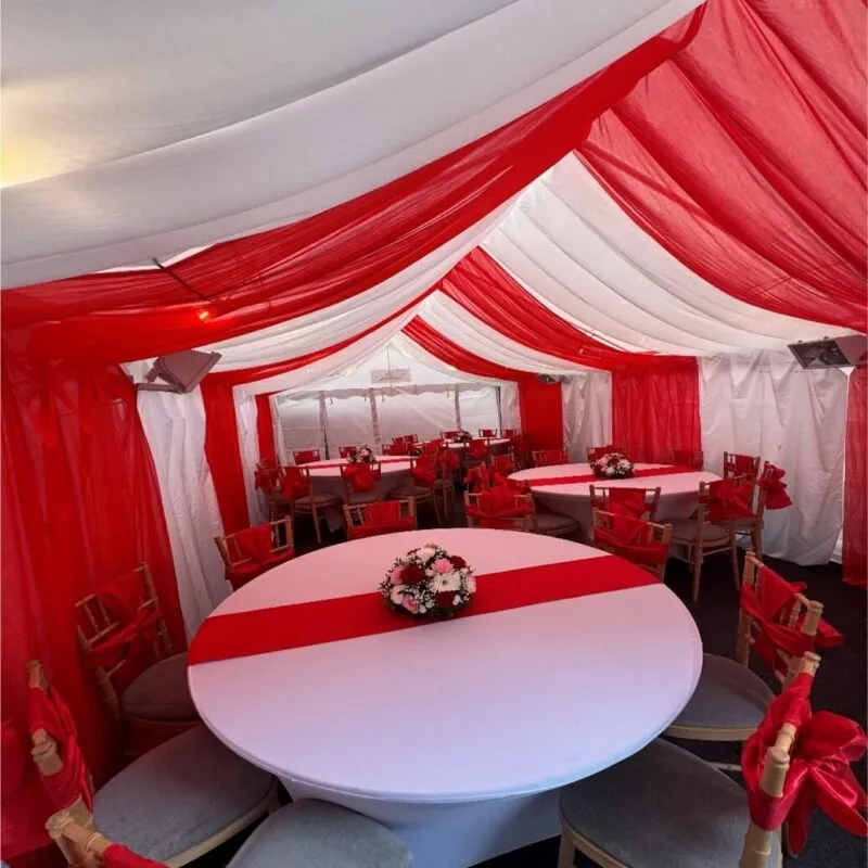 4m x 8m marquee interior in Forest Gate with red and white draped lining, round table layout and Chiavari chairs for family event