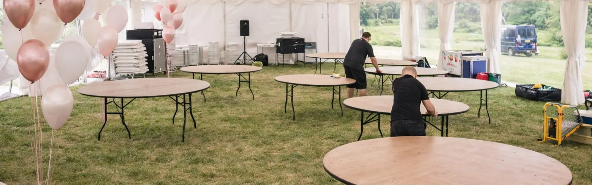 Marquee Event Setup Process Marquee setup in progress with tables on grass showing event planning and preparation