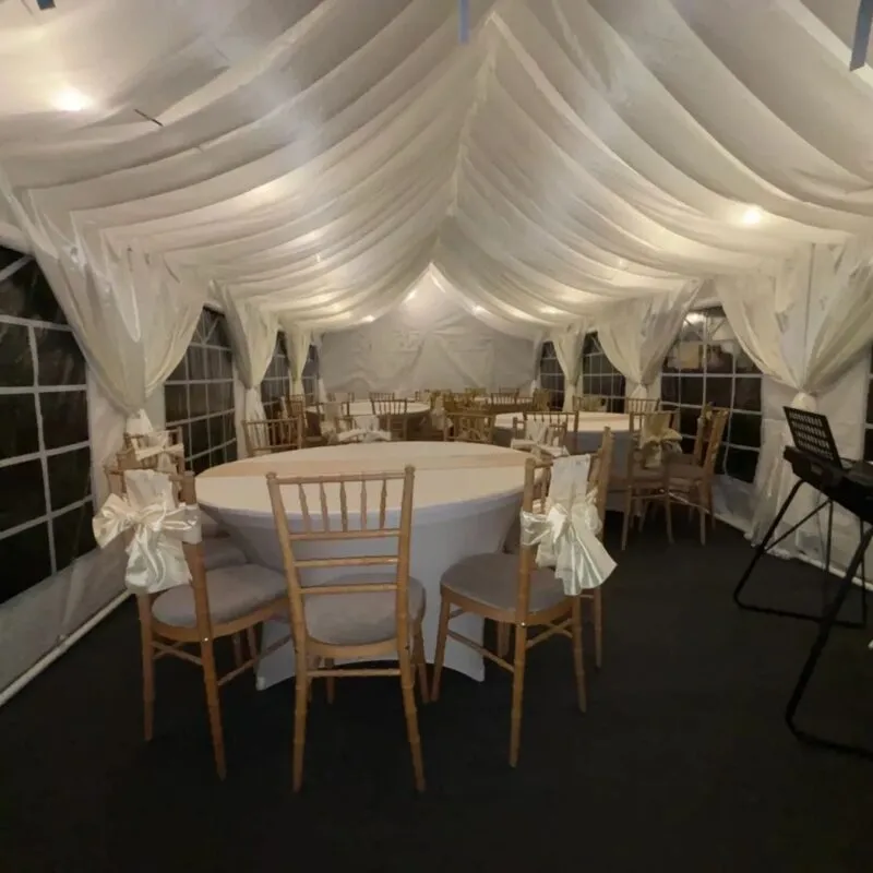 Marquee Hire Essex – Draped Interior Setup Draped marquee interior setup in Essex with round tables and chairs for private event hire
