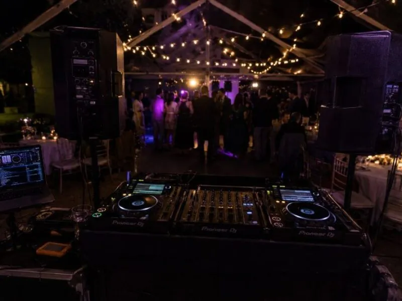 Marquee DJ Hire Evening Party Setup DJ decks, laptop and PA speakers set up inside a marquee with guests, warm lighting and purple party lights